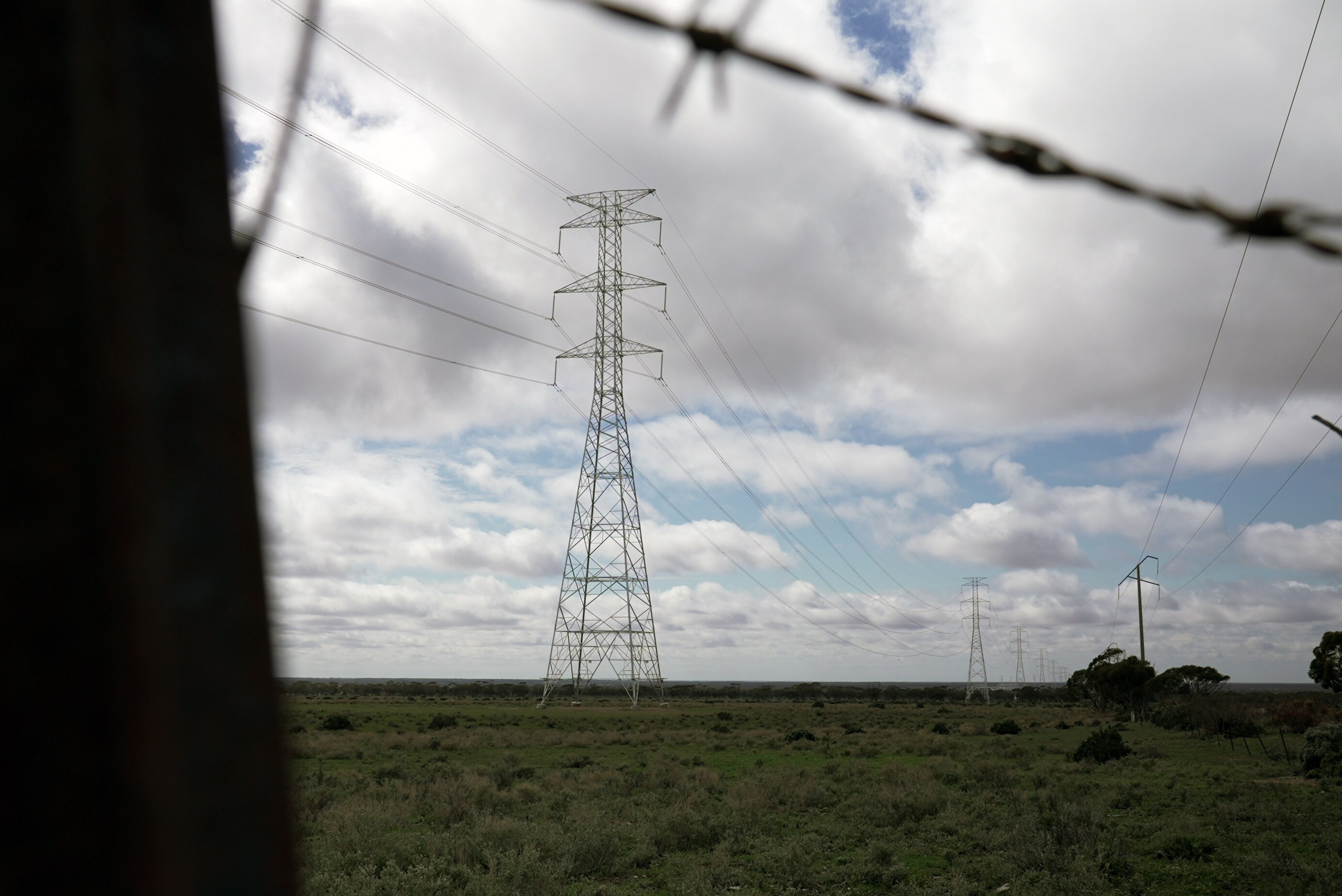 A transmission tower and barbed wire in the foreground