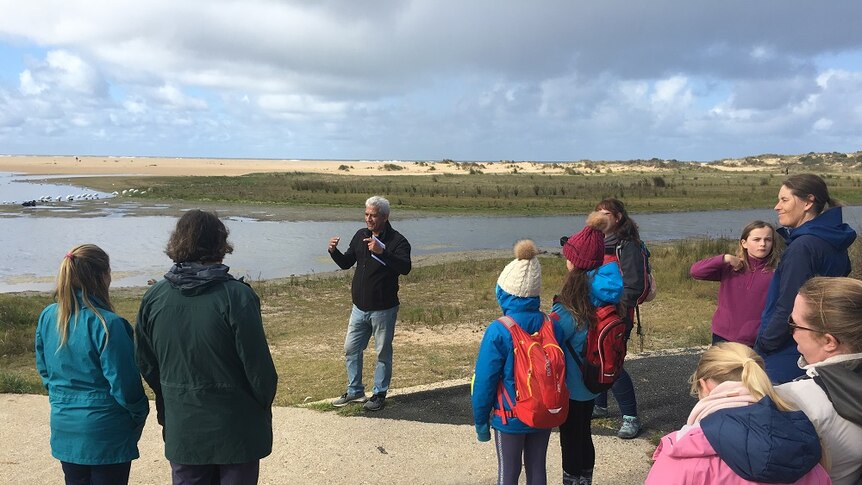 Indigenous elder speaking to a a group of primary school aged children on shoreline of Lake Tyers