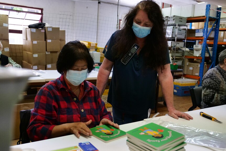 Two women work at a desk wearing blue face masks
