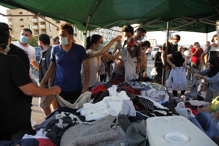 A group of people waring masks gather around a table with clothes on it.