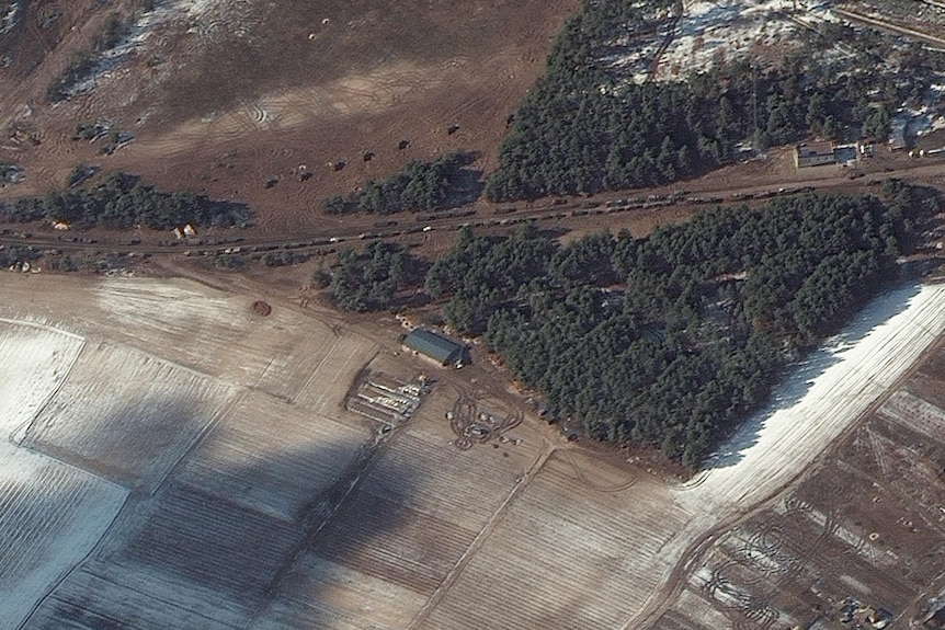 A satellite image shows a long line of army trucks along a rural road