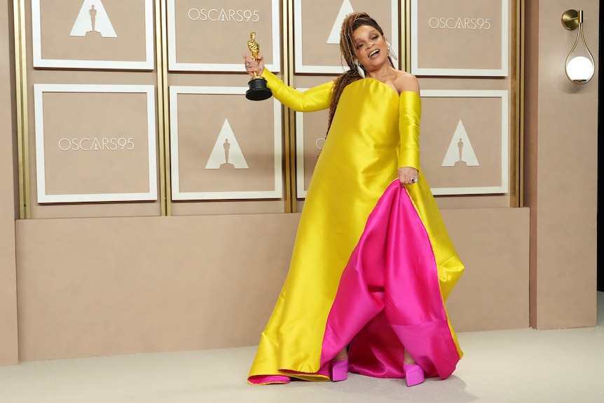 Ruth E Carter in a bright yellow and pink dress holding an Oscar