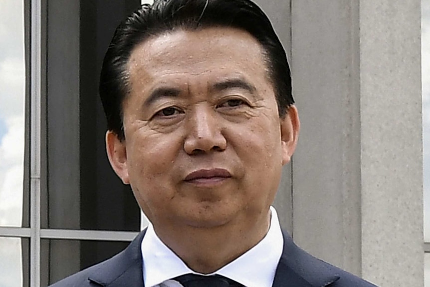 A man wearing a dark blue suit, white shirt and tie in front of a building