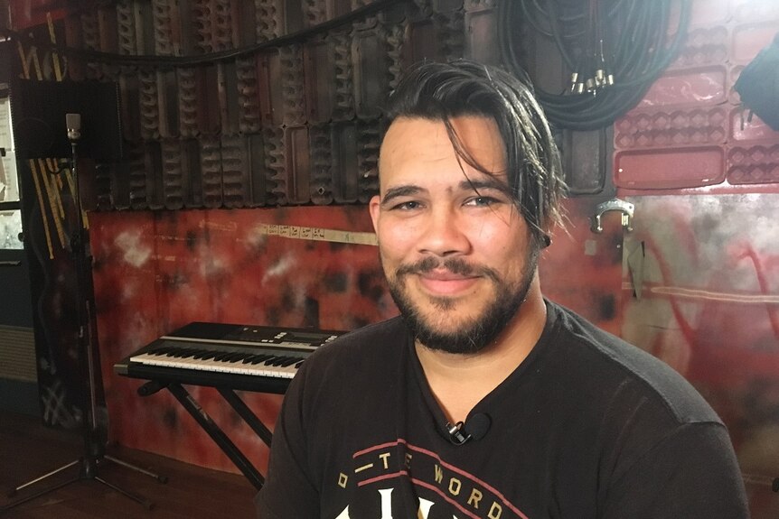 Sean Bahr Kelly sits in a room with a keyboard behind him, wearing a black T-shirt