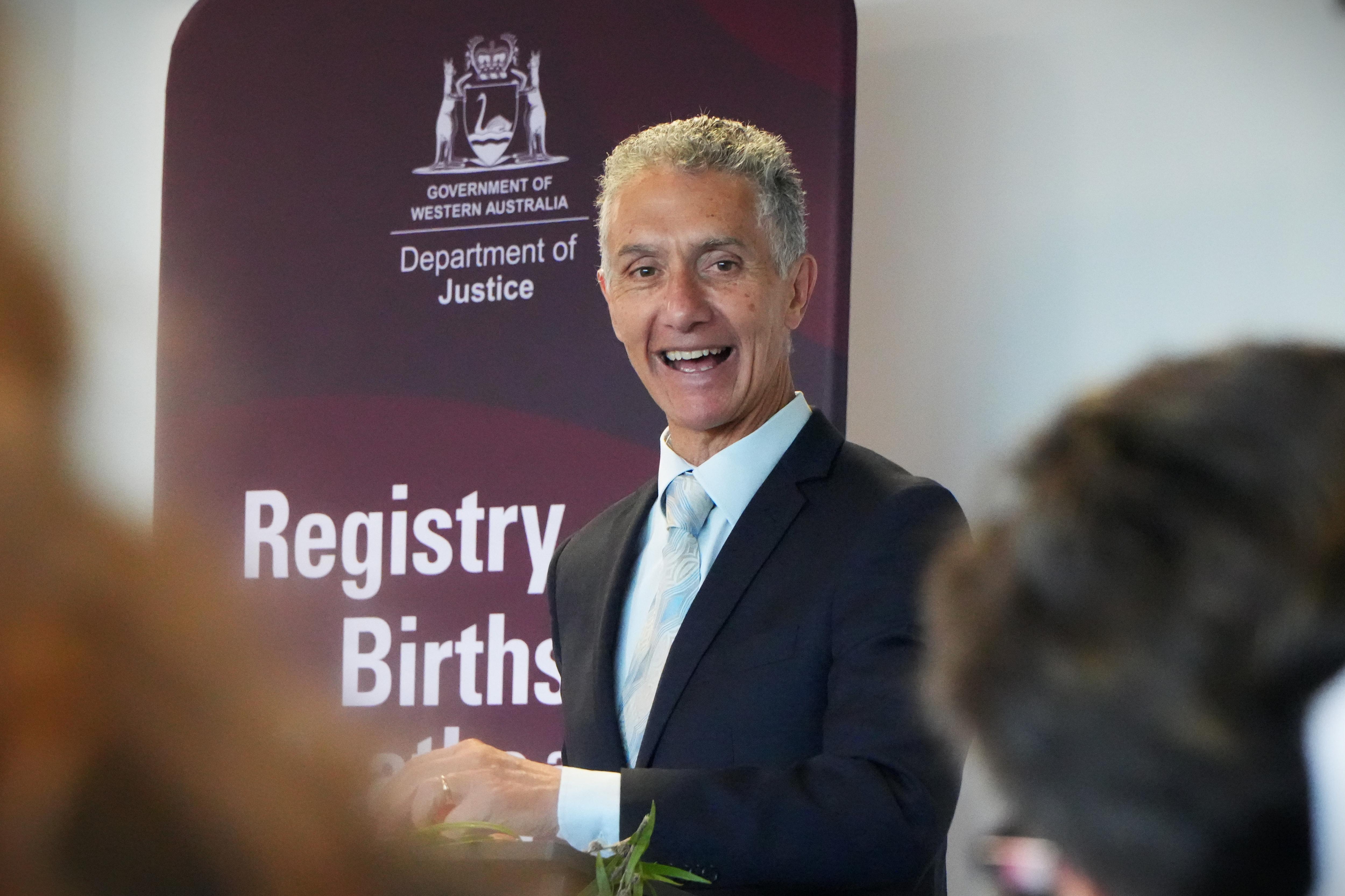 Hombre de traje en medio de un discurso, con un cartel de registro detrás de él