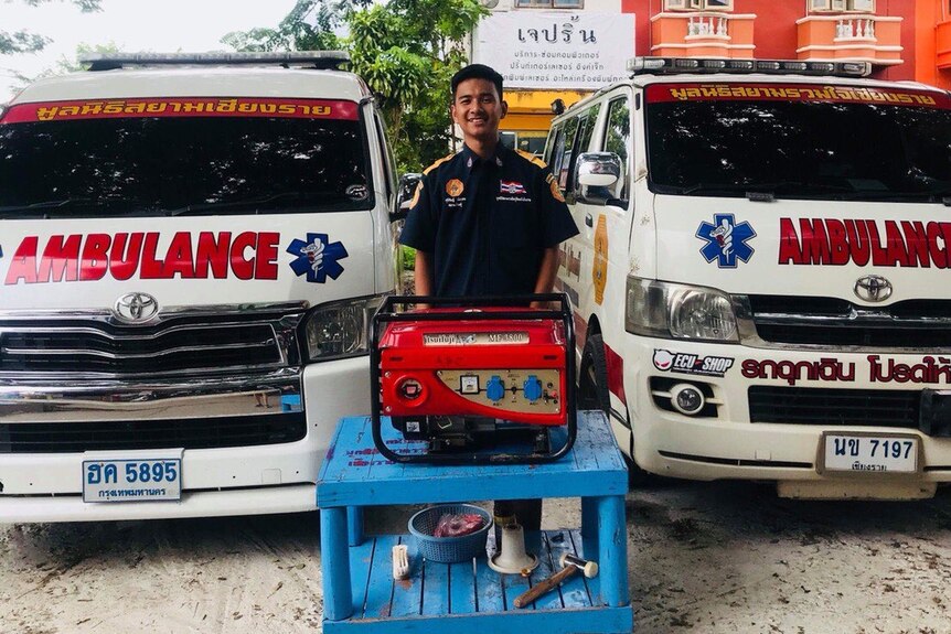 Man in uniform standing between two ambulances in front of generator.