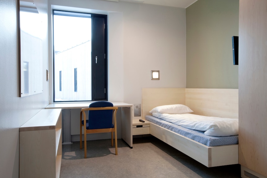 Ein Gefängnis mit Bett, Schreibtisch und Fenster.