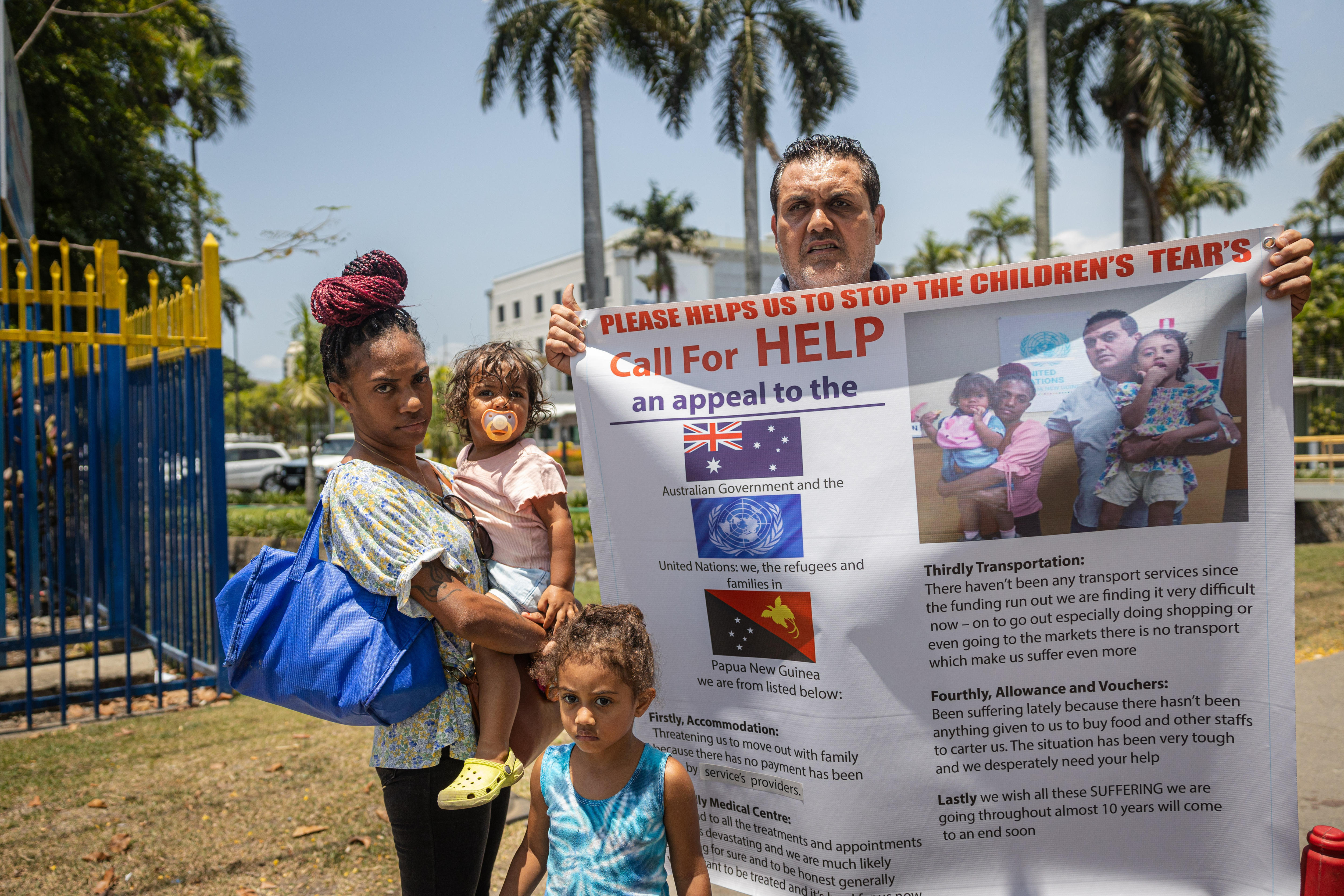 Faisal holds a banner calling for help while his wife and children stand with him 