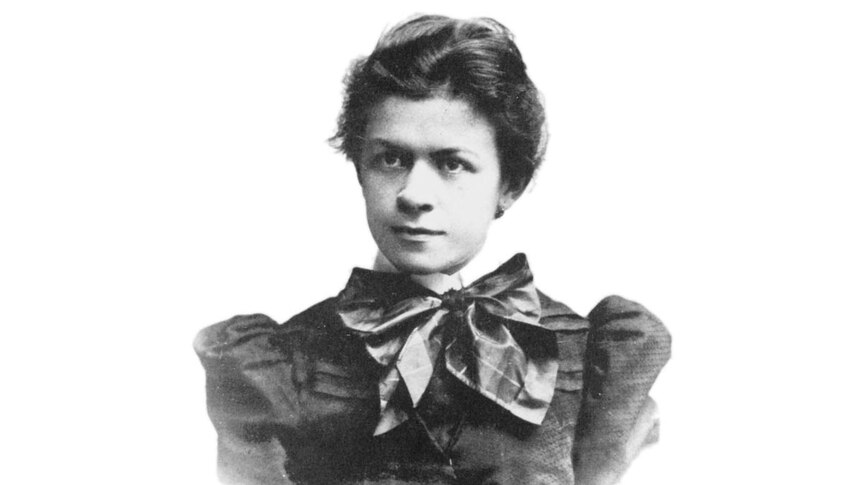 Black and white photo of young woman in black dress with swept-up hair.