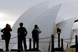 Tourists take photographs and video of the Sydney Opera House from a lookout on the headland known as Mrs Maquarie's Chair.
