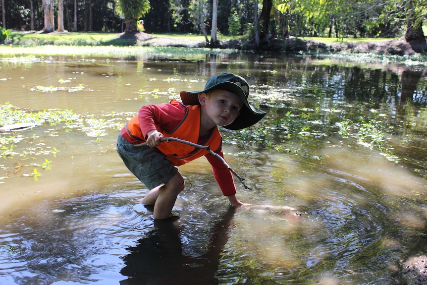 A young boy wades through a muddy dam during a Nature School early education session.