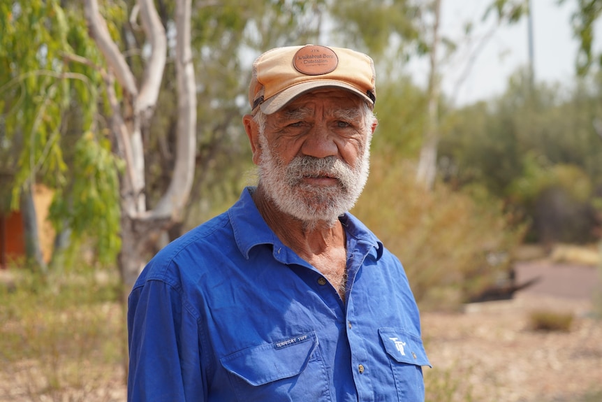 An Aboriginal man stands in front of trees
