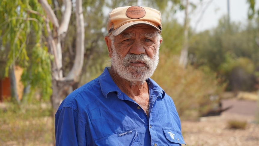 An Aboriginal man stands in front of trees