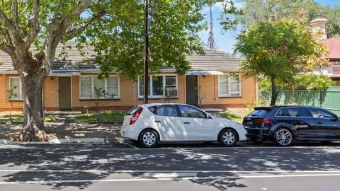 two cars parked on the street in front of cream bricked home