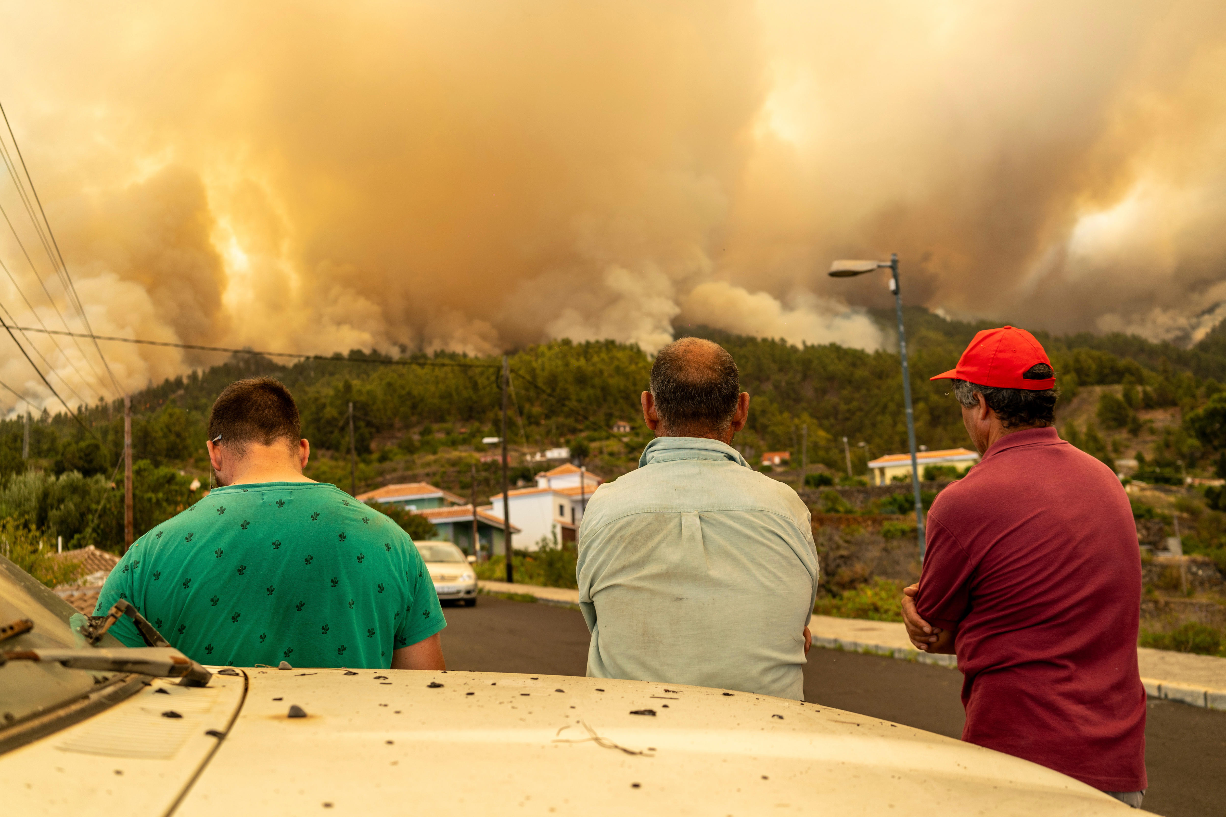 People watch as a fire burns in the distance lighting up the sky orange.