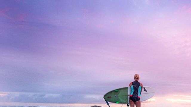A female surfer stands in the shallows holding her board.