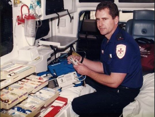 A male with brown hair sorting through medical equipment while in the back of an ambulance. 