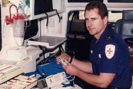 A male with brown hair sorting through medical equipment while in the back of an ambulance. 