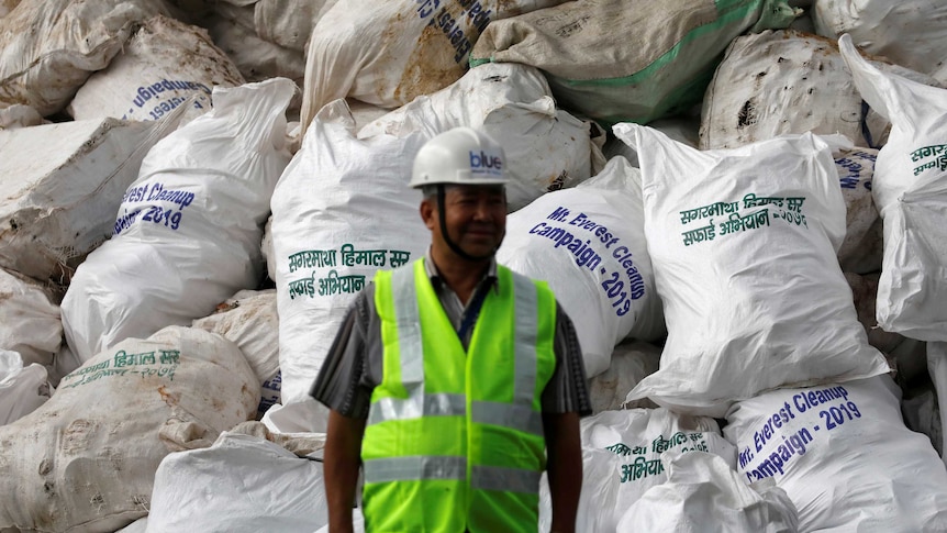 A man stands in front of a pile of garbage in white bags from Mount Everest.