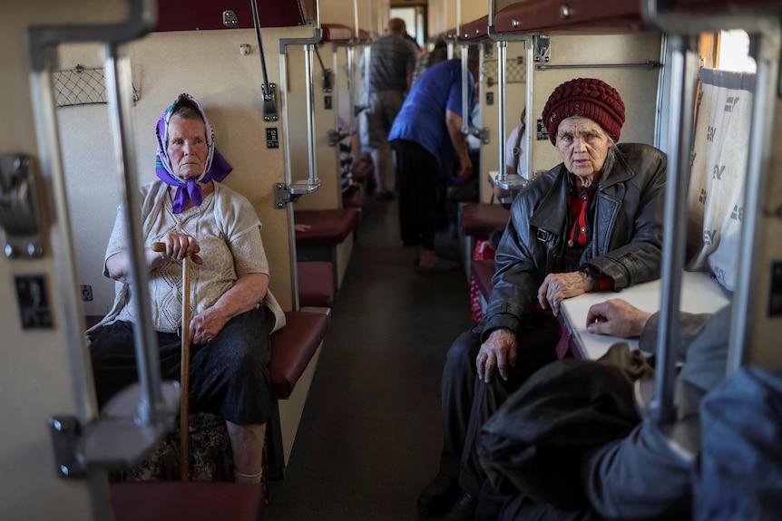 Two elderly women sit inside a train carriage.
