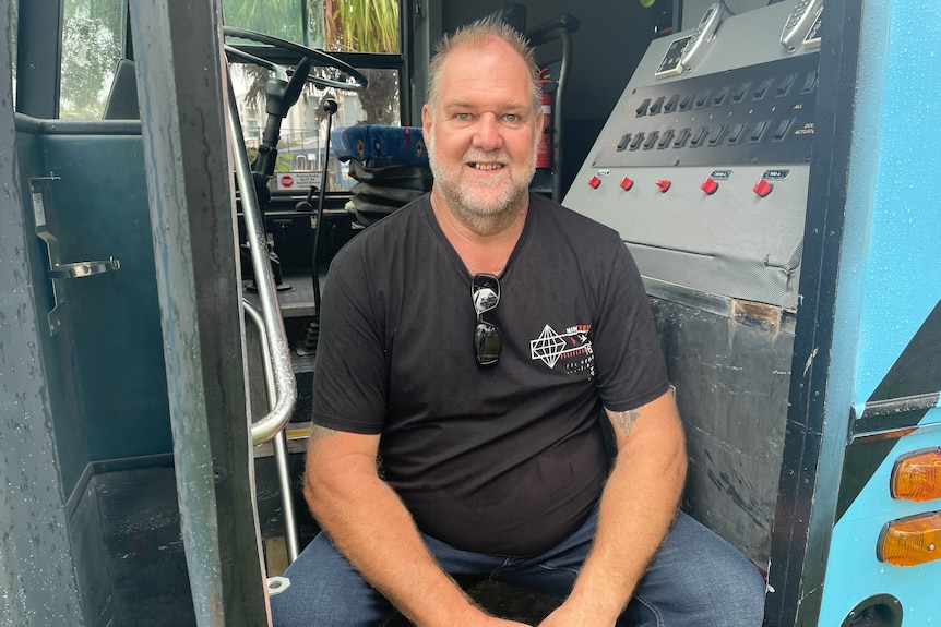 Man smiling, sitting inside door of bus