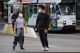 A man and child in a Melbourne street with a tram behind them.
