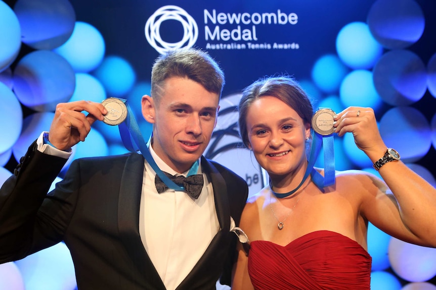 A man in a tuxedo and woman in a red dress hold up medals