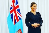 A Fiji minister stands next to a flag.