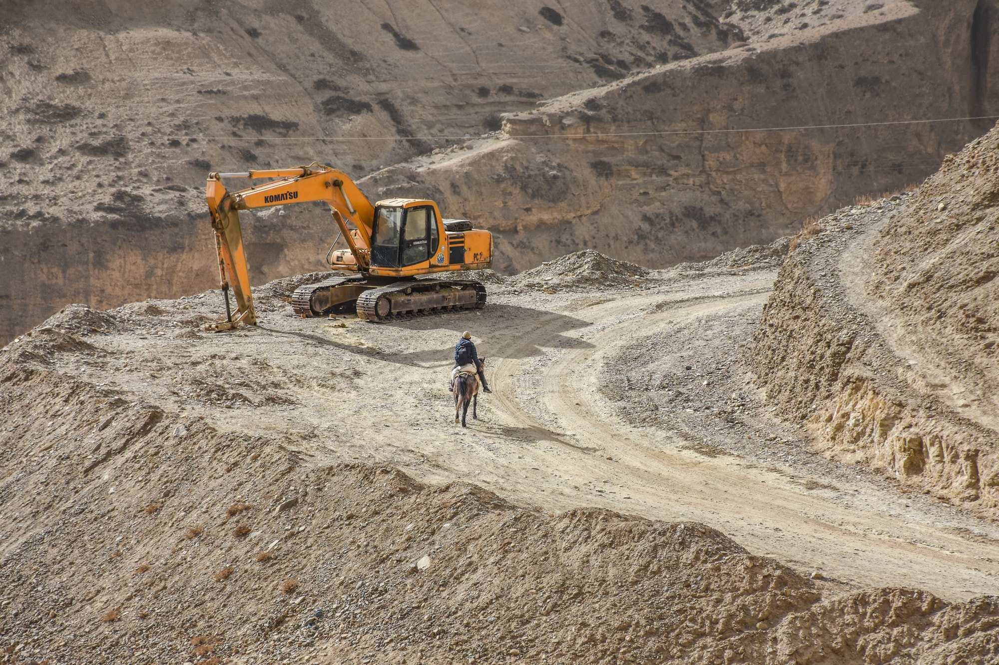 A Loba man on a horse and an excavator side by side on the mountain road