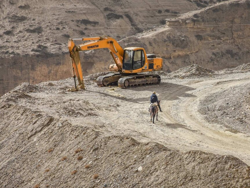 A Loba man on a horse and an excavator side by side on the mountain road