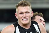 A Collingwood Magpies AFL player holds the ball as he is tackled from behind by a Sydney Swans opponent.