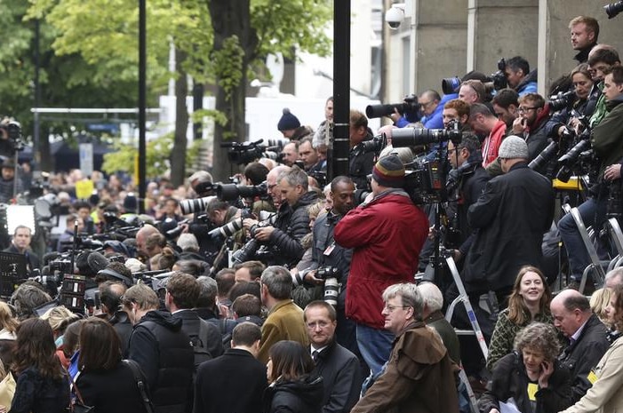 Around 100 photographers wearing predominantly black stan on steps with digital SLR cameras at the ready, pointed at hospital.