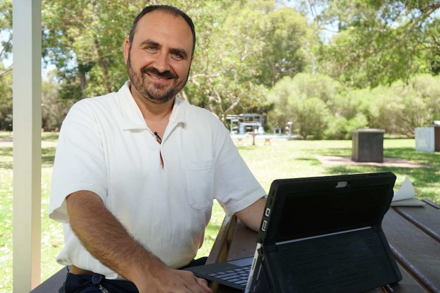 A man wearing office attire sitting at a park table with a laptop