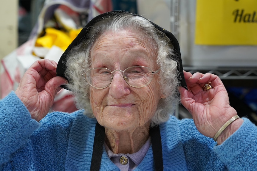 A close up shot of a smiling elderly woman putting a hat on her head 