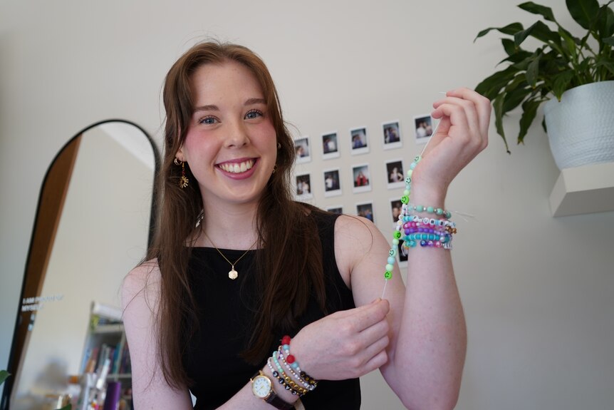 A woman in her early 20s holding up her arm, on her wrist are seven Taylor Swift-themed beaded friendship bracelets