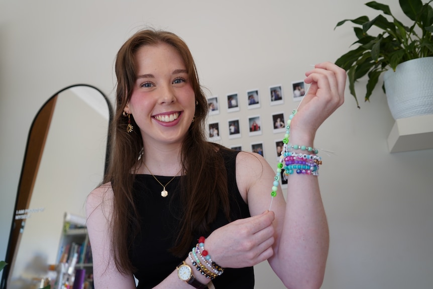 A woman in her early 20s holding up her arm, on her wrist are seven Taylor Swift-themed beaded friendship bracelets