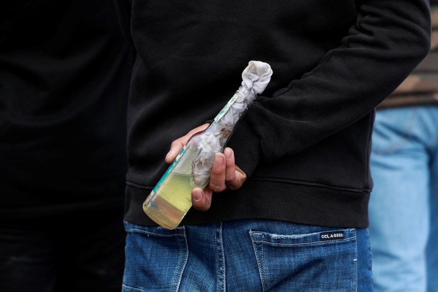 A man holds a molotov cocktail behind his back. 