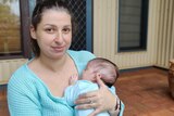 A woman wearing blue, holding a newborn baby.