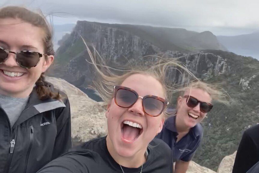 Three women celbrate wildly on a high point above a high coastline