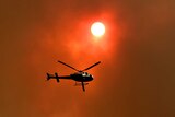 A helicopter silhouetted against a smoky sky.