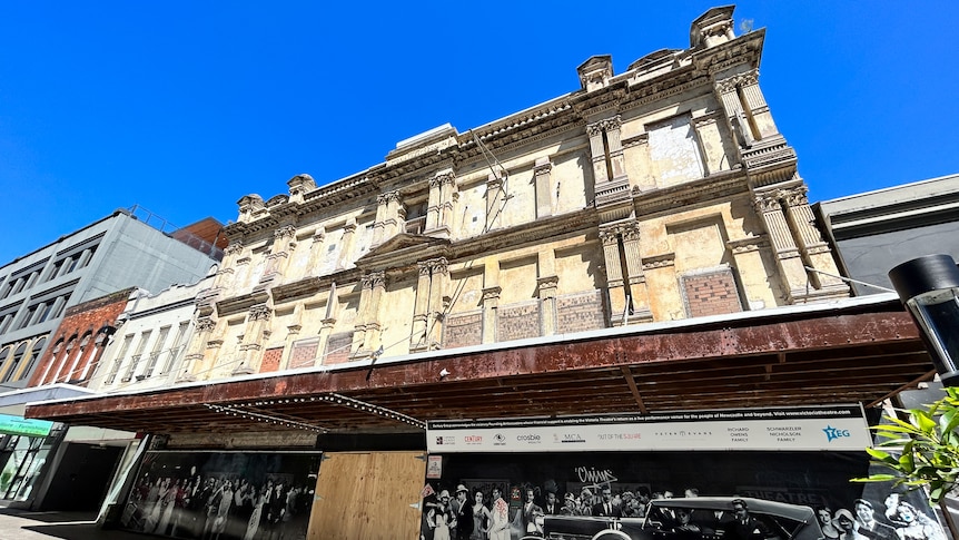 Old cream and tan building boarded up with plywood.