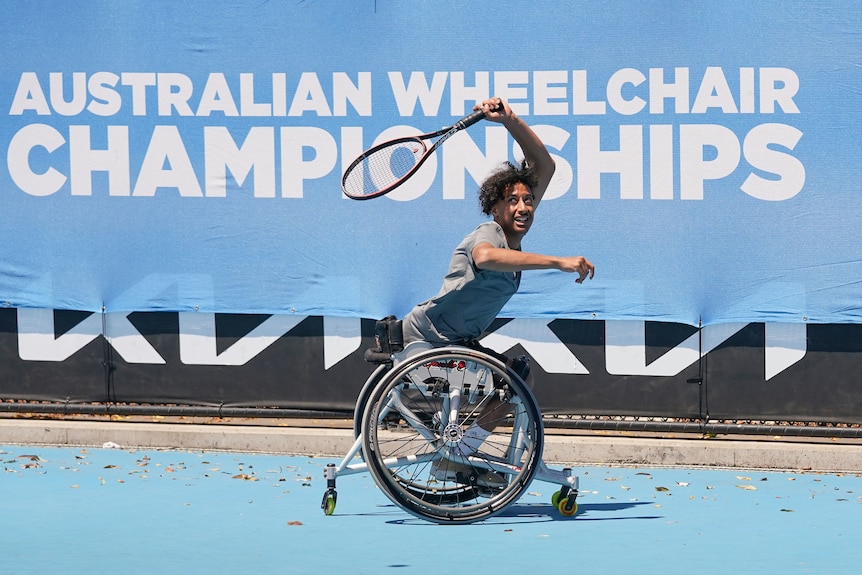 A wheelchair tennis player wheels behind the baseline with his racquet over his head after hitting a return during a game.