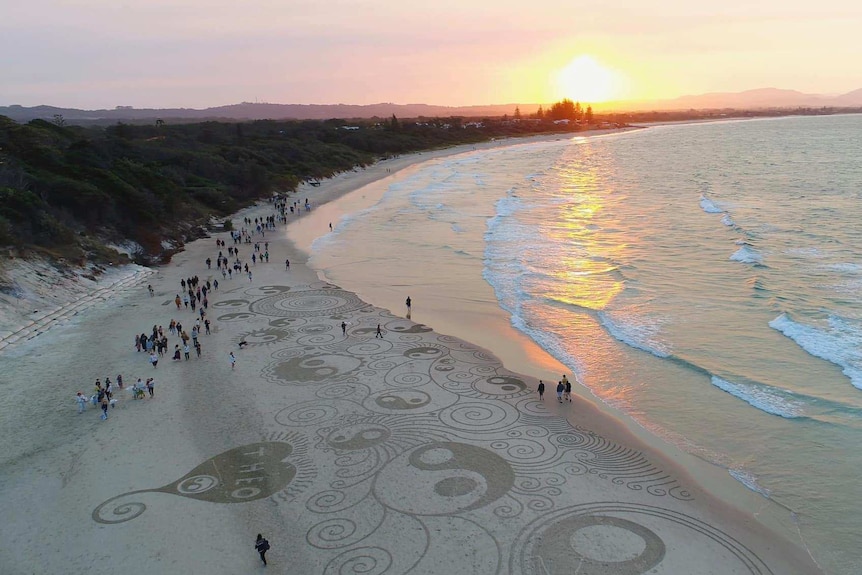 People standing on a beach at sunset.