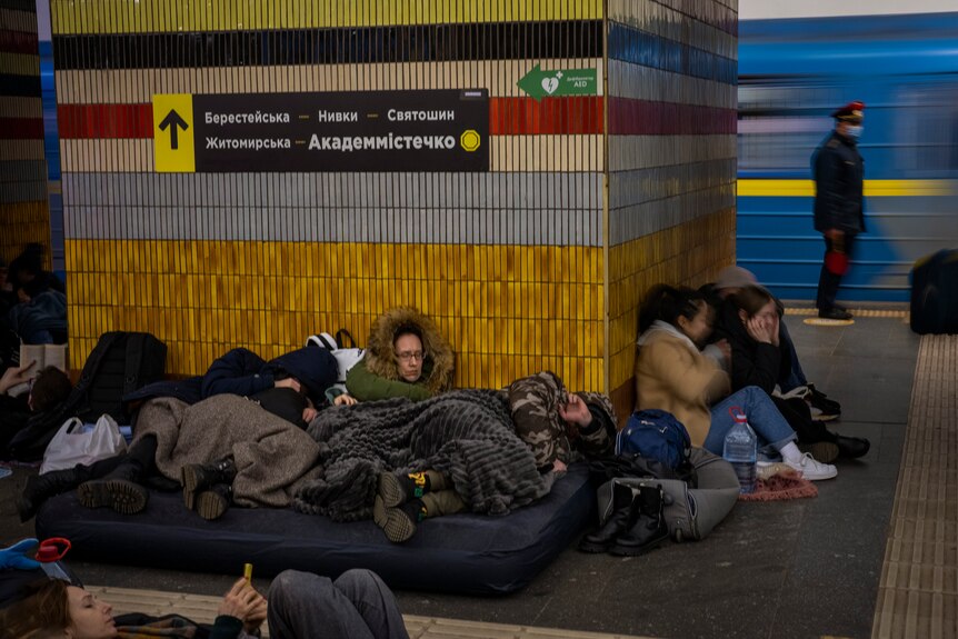 People sleeping on a blow-up mattress, and on the floor of a Kyiv subway station.