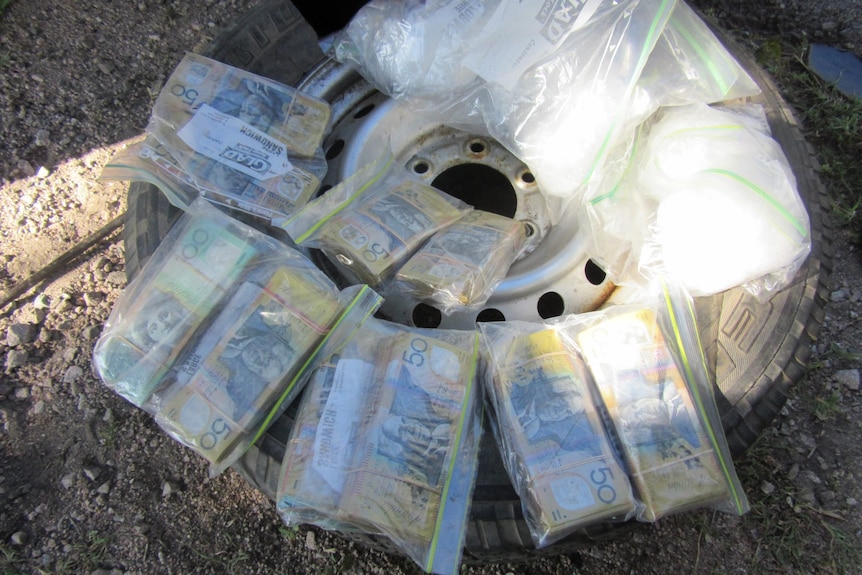 Plastic bags of cash and drugs sitting on top of a car tyre.