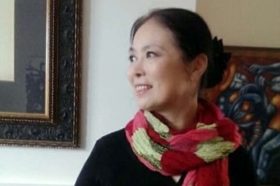 A Chinese woman wearing a black jumper and a scarf looks off to the side inside a gallery-like room.