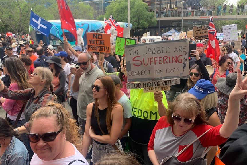 A large crowd of people holding placards protesting COVID vaccines.