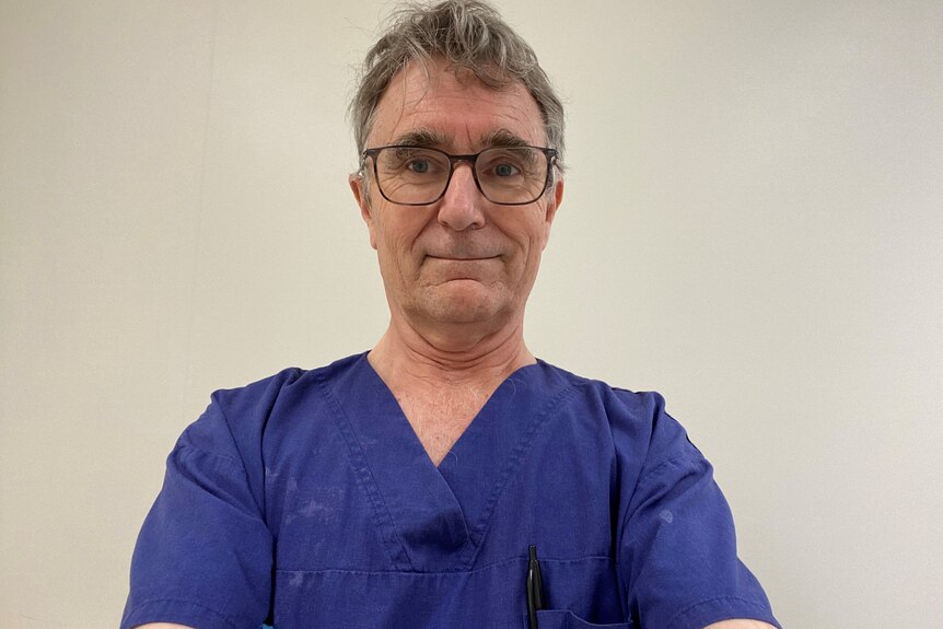An image of Dr Graeme Siggs in blue scrubs in front of a white wall