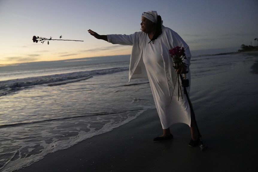 Woman throws flower into the ocean to honour her African ancestors.