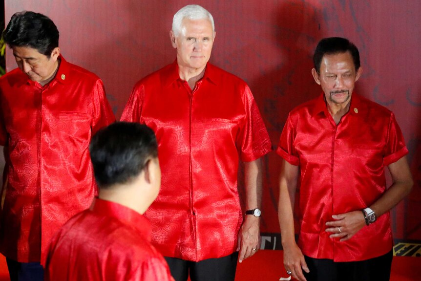 Mike Pence looks at Xi Jinping, whose face is obscured. Everyone is wearing matching red shirts.